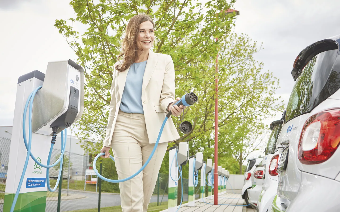 E-Mobilität - Kundin vor Ladestation mit Stecker in der Hand &middot; ABE Elektrotechnik